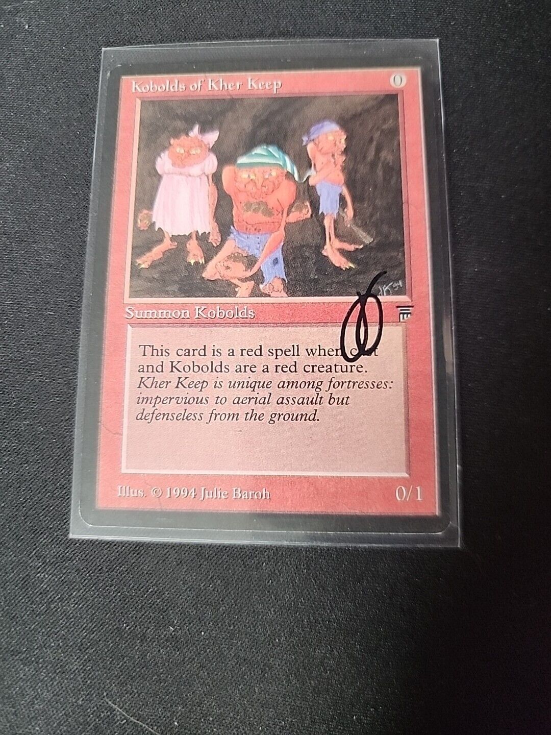 A collectible card from Wizards of the Coast's Magic: The Gathering, showing three whimsical creatures titled "Kobolds of Kher Keep SIGNED Julie Baroh" with game stats and description text, encased in a protective sleeve on a black background.