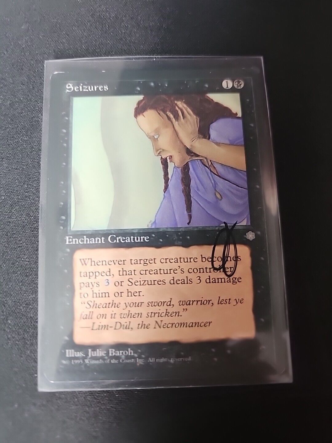 A protected Magic: The Gathering card, "Seizures SIGNED Julie Baroh," featuring an illustration of a distressed woman clutching her head, displayed on a black surface. The card text and details are partially visible. (Wizards of the Coast)